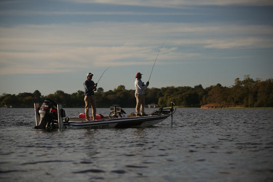 Two anglers bass fishing from a boat on a lake at sunrise