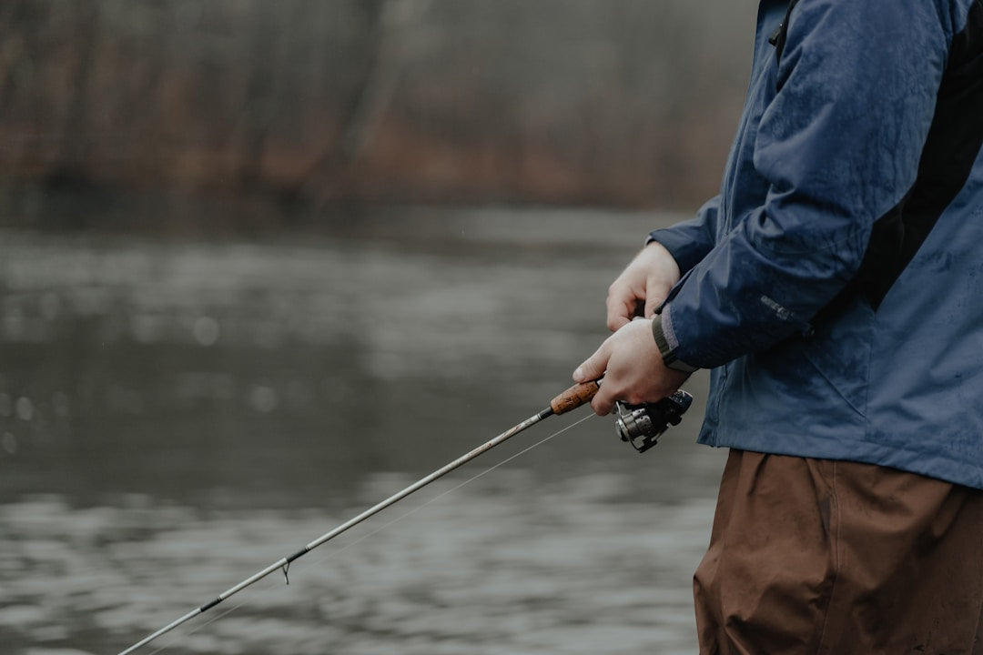 Beginner angler holding a fishing rod beside a calm lake, ready to fish for the first time