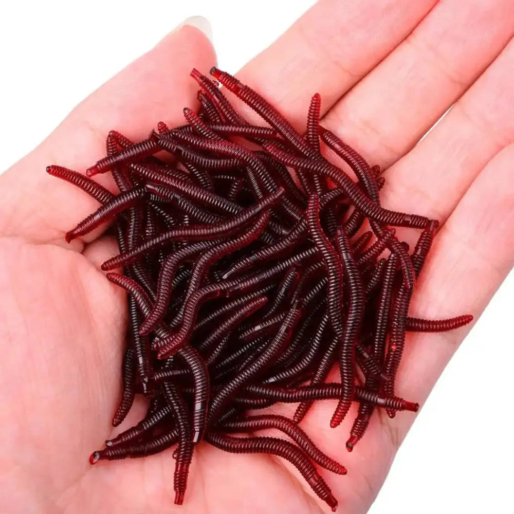 A hand holding multiple artificial earthworms for fishing in various shades of red, ideal for attracting fish.