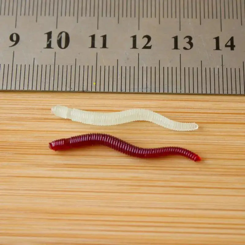 Two artificial earthworms for fishing, one red and one translucent, displayed with a ruler for size reference