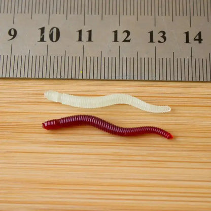 Two artificial earthworms for fishing, one red and one translucent, displayed with a ruler for size reference