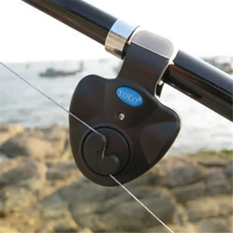 Audible fishing alarm attached to a fishing rod with a scenic waterfront background